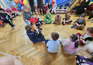 Bal Karnawałowy - dzieci bawią się kapeluszem siedząc w kręgu