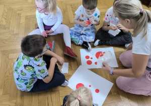 piątka dzieci siedzi na podłodze i przykleja do kartonu kropki