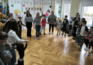 Dzieci stoją w kole i podnoszą ręce i nogi na znak nauczyciela