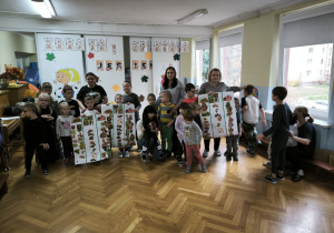 Dzieci prezentują prace - przyklejone liście na dużych kartonach papierowych