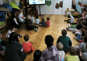 Dzieci siedzą na podłodzie i oglądają krótki film edukacyjny o piramidzie żywieniowej