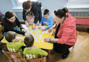 Dzieci z Przedszkola Miejskiego 109 oraz Przedszkola Miejskiego 221 rywalizują w grach planszowych siedząc przy stoliku wraz z opiekunkami