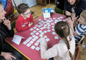 Dzieci z Przedszkola Miejskiego 214 oraz Przedszkola Miejskiego Specjalnego nr 1 rywalizują w grach planszowych siedząc przy stoliku wraz z opiekunkami
