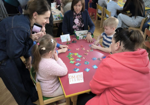 Dzieci z Przedszkola Miejskiego 109 oraz Przedszkola Miejskiego Specjalnego nr 1 rywalizują w grach planszowych siedząc przy stoliku wraz z opiekunkami