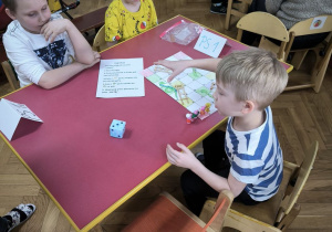 Dzieci z Przedszkola Miejskiego Specjalnego nr 1 rywalizują w grach planszowych siedząc przy stoliku wraz z opiekunkami