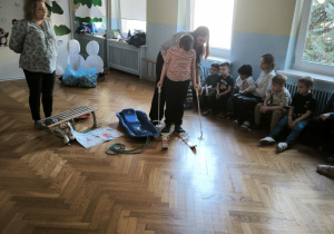 Chłopiec w białej bluzce w paski trzyma kijki i przymierza narty