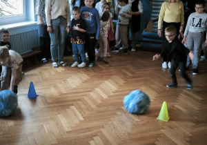 Dzieci turlają po ziemi niebieskie kule pokonując slalom