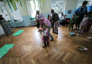 Dziewczynka przebrana za motyla niesie kwiatka, aby umieścić go na podłodze, na zielonym kartonie