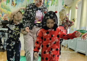 Chłopcy z grupy Pszczółek spacerują z nauczycielką po zielonym płótnie. Wokół dzieci latają mydlane bańki