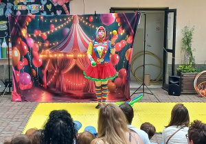 Pani przebrana za clowna żongluje kolorowymi piłkami