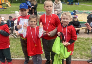 Dzieci z grupy "Zajączkow" ubrane w czerwone koszulki stoją z medalami na szyjach