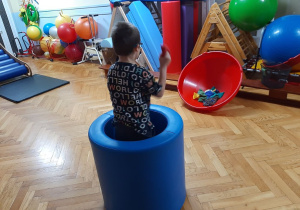 Chłopiec stoi w środku tunelu rehabilitacyjnego i rzuca woreczkami do celu