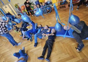 Dzieci leżą na plecach i kopią balon zawieszony na linie