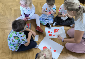 piątka dzieci siedzi na podłodze i przykleja do kartonu kropki