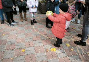 Chłopiec w czarnej czapce, czerwonej kurtce trzyma w rękach kolorową piłkę