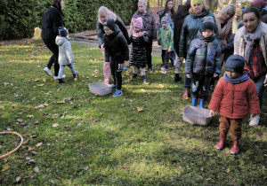 Dzieci stoją na trawie i szykują się do wrzucania kasztanów do kół położonych na trawie