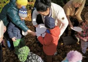 Dzieci stoją na opadłych liściach i przerzucają kasztana z talerza na talerz