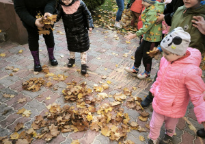 Dwie dziewczynki wrzucają liście do koła namalowanego na kostkach brukowych