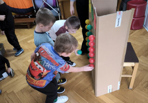 Trzech chłopców przykleja kolorowe - żółte, zielone i czerwone kule do tekturowego kartony
