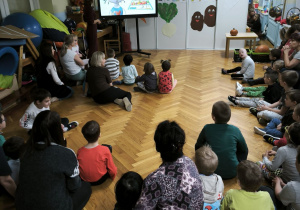 Dzieci siedzą na podłodzie i oglądają krótki film edukacyjny o piramidzie żywieniowej