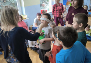 Chłopiec mając zasłonięte oczy próbuje zgadnąć jakie owoce i warzywa podaje mu nauczycielka