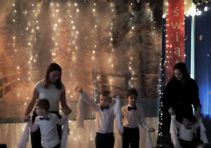 Dzieci z grupy Tygrysków występują przed rodzicami, trzymają ręce w górze. Do nadgarstków mają przyczepione białe chusty