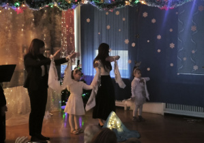 Dzieci z grupy Puchatków występują przed rodzicami, trzymają ręce w górze. Do nadgarstków mają przyczepione białe chusty