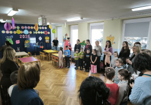 Dzieci z przedszkoli stoją w sali gimnastycznej, czekając na rozpoczęcie olimpiady