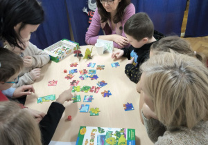 Dzieci z Przedszkola Miejskiego 36 oraz Przedszkola Miejskiego 214 rywalizują w grach planszowych siedząc przy stoliku wraz z opiekunkami