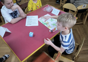 Dzieci z Przedszkola Miejskiego Specjalnego nr 1 rywalizują w grach planszowych siedząc przy stoliku wraz z opiekunkami