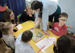 Dzieci z Przedszkola Miejskiego 185 oraz Przedszkola Miejskiego 214 rywalizują w grach planszowych siedząc przy stoliku wraz z opiekunkami