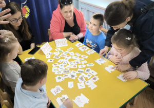 Dzieci z Przedszkola Miejskiego 109 oraz Przedszkola Miejskiego 185 rywalizują w grach planszowych siedząc przy stoliku wraz z opiekunkami