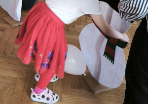 Dziewczynka przyczepia elementy ubioru do postaci bałwana