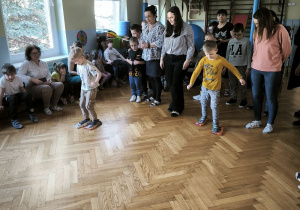 Dzieci ścigają się w sali przesuwając stopy po parkiecie na specjalnych, papierowych butach zrobionych z gazet