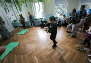 Chłopiec przebrany za żabkę niesie kwiatka, aby umieścić go na podłodze, na zielonym kartonie