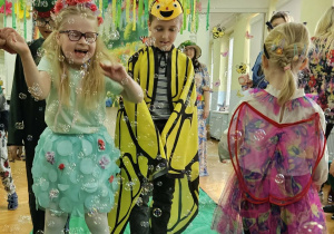 Dzieci z grupy Zajączków spacerują po zielonym płótnie. Wokół dzieci latają mydlane bańki