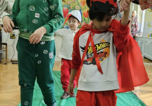 Chłopcy z grupy Misiów spacerują po zielonym płótnie. Wokół dzieci latają mydlane bańki