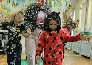 Chłopcy z grupy Pszczółek spacerują z nauczycielką po zielonym płótnie. Wokół dzieci latają mydlane bańki