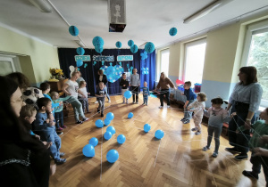 Dzieci stoją w kręgu i trzymają niebieską nić tworzącą "pajęczynę"