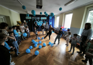 Dzieci stoją w kręgu i kopią leżące na podłodze, niebieskie balony