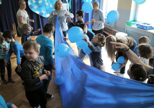 Dzieci podbijają balony ponad rozciągniętym niebieskim płótnem