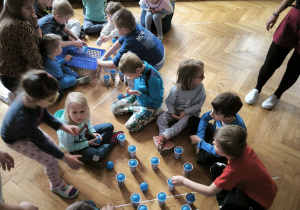 Dzieci wkładają do leżących na podłodze kubków niebieskie piłki
