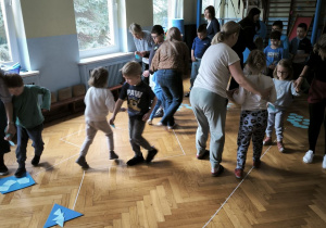 Trzy grupy dzieci pokonują tor i kładą na podłodze wycięte z papieru figury geometryczne