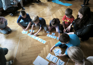 Dzieci siedzą na podłodze i układają z liter wyraz "autyzm"