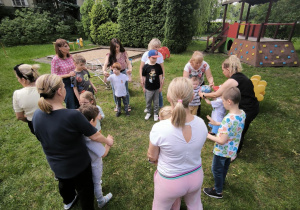 Dzieci stoją w kółku i przekazują sobie piłkę z rąk do rąk