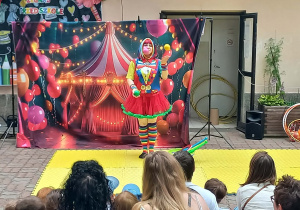 Pani przebrana za clowna żongluje kolorowymi piłkami