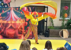 Pani przebrana za clowna wymachuje żółto - pomarańczowymi chustami
