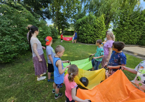 Dzieci stoją i trzymają chusty z umieszczonymi w środku piłkami